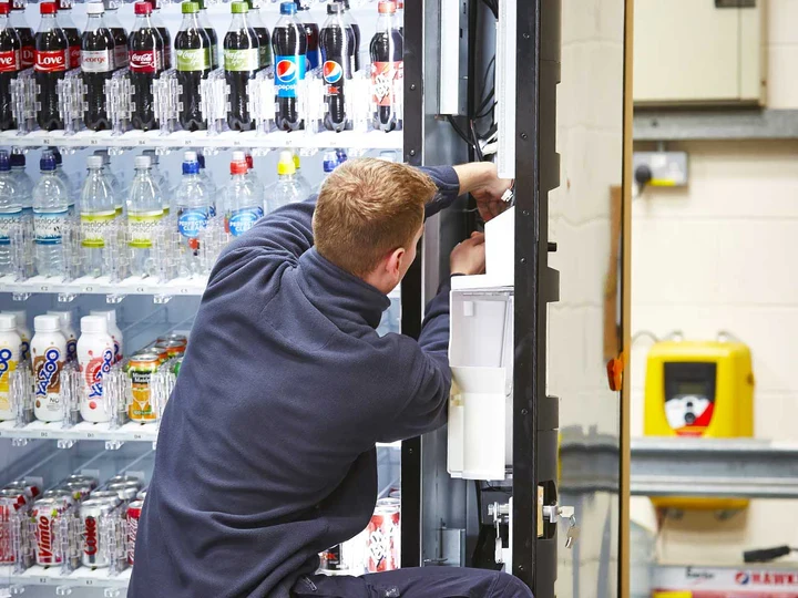 A technician working inside the open door of a stocked drinks machine during installation