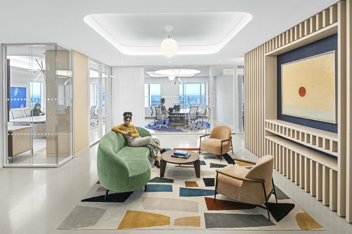 A modern office breakout lounge with soft seating, where staff work and meet between desks and a glass-walled boardroom
